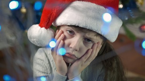Child feeling lonely at Christmas. A little girl in Santa hat feeling lonely in the room with Christmas atmosphere.