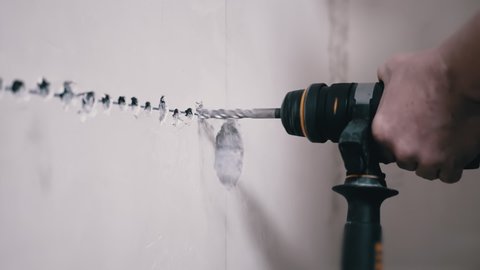A Builder Using a Puncher Makes a Hole in a Concrete Wall to Install an Outlet. Rotation of a drill on an electric rotary hammer. Lots of flying cement dust. Installation of electrical wiring at home.