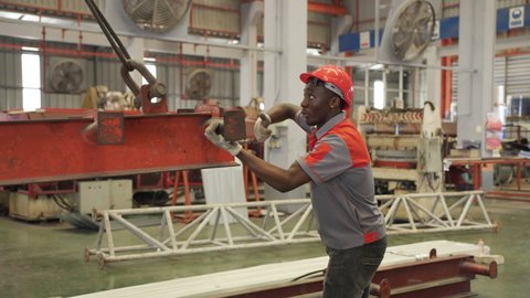 Industrial African workers give hand signals to lift steel bars with slings or electric hoists.