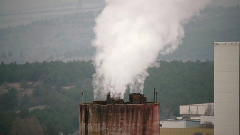 8K 7680x4320.Industrial chimney polluting air.Industry roof with chimneys polluting the atmosphere at a cloudy day.Damage to nature through factory.Forest building global warming toxic waste sad smoke