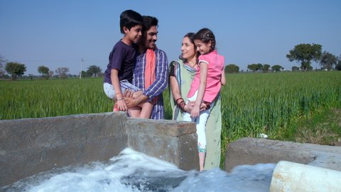 Cheerful villagers hugging their little kids while standing near a tubewell - parent-child bonding, love and affection. A happy family of an Indian village - village lifestyle, Indian agriculture, ...