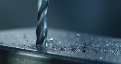 Macro shot of tip of drill machine drilling hole with circular motion with silver metal shavings during steel machining process in heavy industry factory.