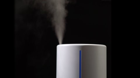 Household humidifier. White electronic device for humidification, ionization and air purification. White water vapor. Steam on a black isolated background.