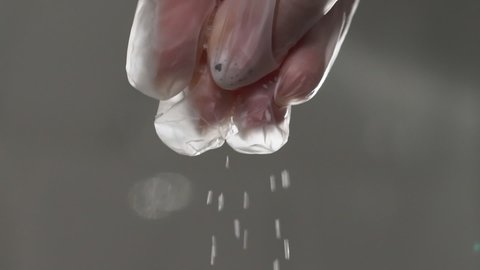 Woman cook in gloves salts food. Cooking, seasoning. Sea coarse salt is poured in slow motion. Macro close up shot of person at the kitchen. Sugar or spice falling down.