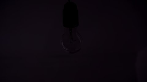 A lamp with a tungsten bulb assembly slowly turns on and off on a black background, a close-up shot of an old retro-vintage light bulb brightening the light. A comfortable cozy concept.