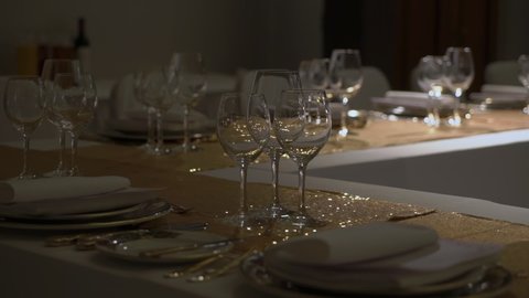 Holiday dinner in restaurant. Decorated hall for reception, celebration party, wedding, anniversary or birthday. White tables with no food. Golden tablecloth decoration. Glass and plates empty.