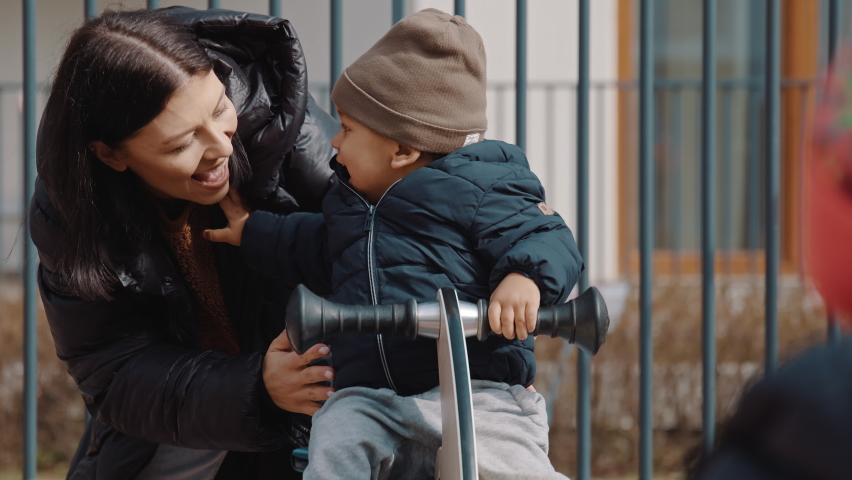 excited little boy wearing grey hat black coat and grey trousers sitting on a see-saw and laughing medium shot outdoor. High quality 4k footage