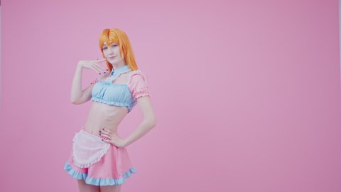 young female model posing and touching her hip wears crop top and short pink skirt with apron isolated medium long studio shot. High quality 4k footage