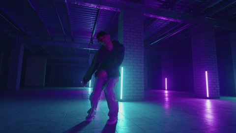 A steel man dances hip-hop freestyle in a modern style in a hall with neon light in purple blue colors. Male Professional Hip Hop Dancer
