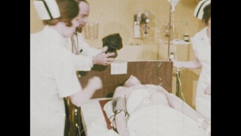 1970s: Nurse starts chest compressions on a patient while the doctor uses a bag valve mask. Another doctor rolls in a defibrillator. He borrows a stethoscope to check the patient.