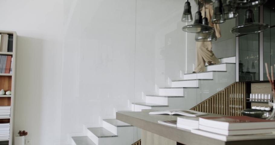 Slow motion photo of a young independent Caucasian woman descending the stairs in her modern duplex apartment. female legs descending the minimalist stairs. Barefoot woman descends a modern staircase. Royalty-Free Stock Footage #1088995539