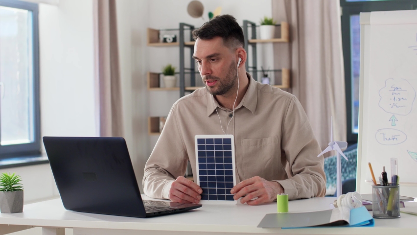 Distance education, school and green energy concept - male teacher with laptop and solar battery model having online class at home office | Shutterstock HD Video #1088995909