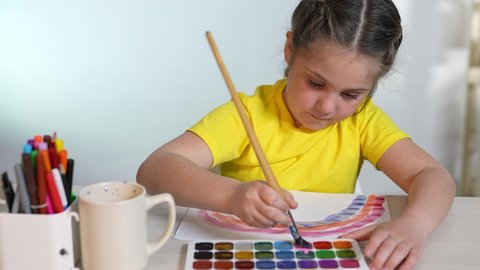 Child girl drawing a rainbow. child artist draws indoor at the table in kindergarten. coronavirus pandemic stay home concept. kid draws a rainbow. school kindergarten drawing lesson