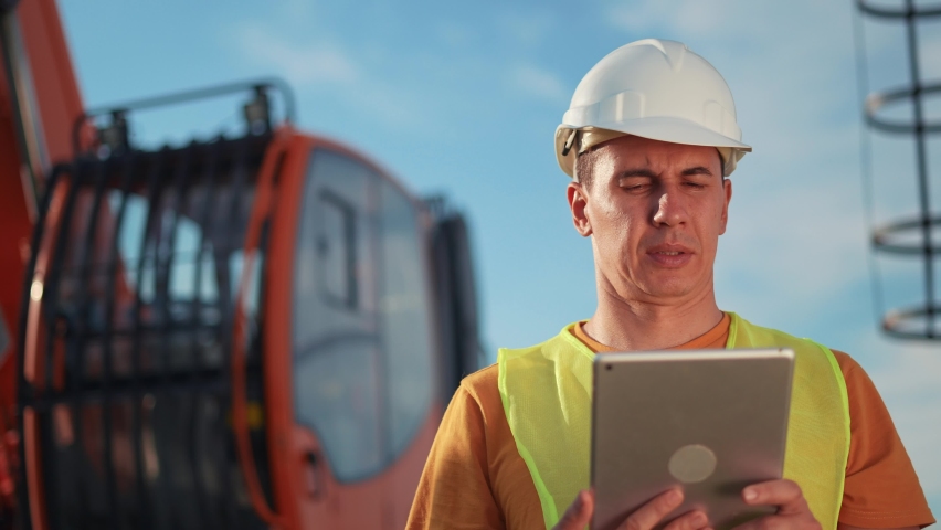 worker in hard a hat with digital tablet near excavator. construction site driver with digital tablet. industry construction concept. business worker in hard hat near excavator truck in uniform. Royalty-Free Stock Footage #1088998213