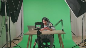 A Camera Recording Asian Man Gamer With Headphone And Computer Waving Hand While Playing Game On Mobile Phone On Green Screen With Professional Light Equipment

