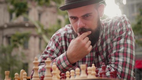 Spanish man playing chess outdoor. Latin bearded guy moving chess figures on a wooden checkered board. Strategy and thinking, brainstorming. 