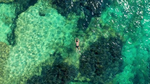 Aerial view of unrecognizable people snorkeling above coral reef reaching deeper parts of the crystal clear water, Corfu, Greece. Aerial drone view of a couple snorkeling swimming in crystal clear wat
