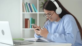 Happy teen schoolgirl wearing headphones reading good news online on smartphone, distance learning online remote lesson class at home. Distance education concept. 4k footage