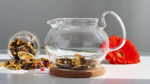 Pour hot water from an electric kettle into a glass teapot with fruit tea. Green tea with fruits is brewed in boiling water. The tea leaves swirl from the movement of water. A spill of tea on the tabl