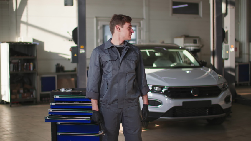 portrait of a happy young man in uniform with tools in his hands working in a car service as a mechanic, smiling and looking at the camera Royalty-Free Stock Footage #1089002685