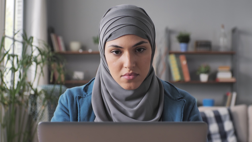 Muslim female entrepreneur upset stressed sits at the desk working at computer reading bad news,arab woman works at the laptop frustrated having problem | Shutterstock HD Video #1089006409