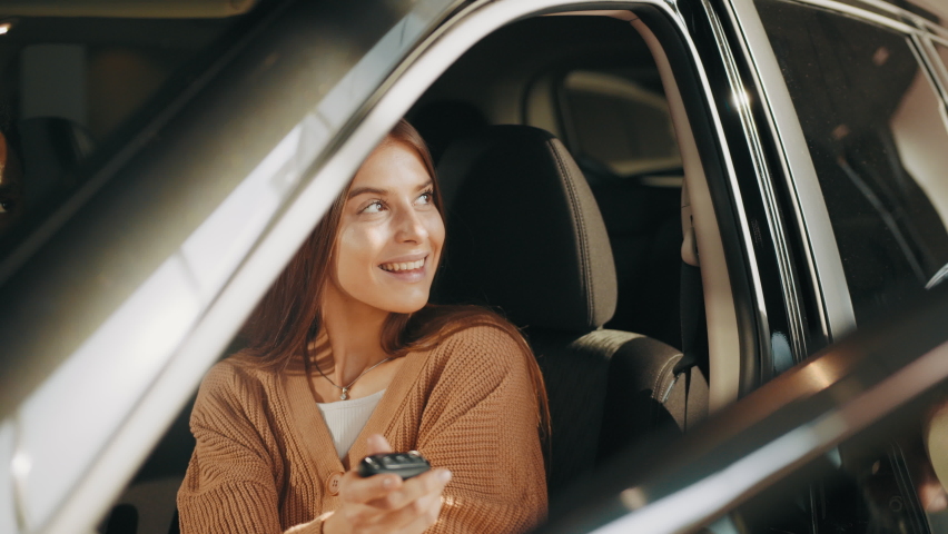 Happy woman taking car key from dealer in auto show or salon. Car dealer giving key to new car owner. Woman receiving car keys from a dealer. Choosing of new vehicle. Concept of expensive purchase