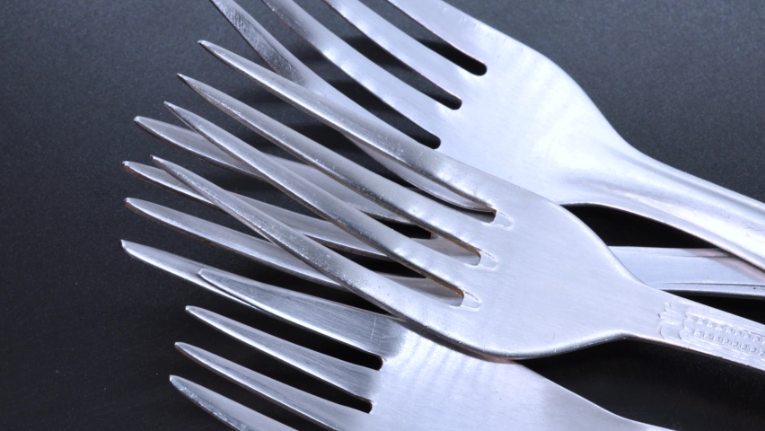 Macro shot of four steel forks on a black bacground, rotating motion. Close up view from above.