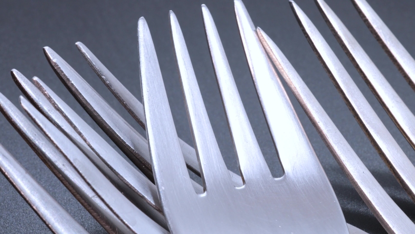 Close up view of four steel forks on a black bacground, rotating motion. Close up view from above.