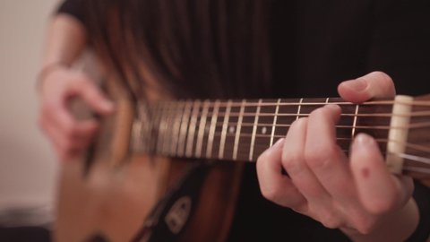 Acoustic guitar fretboard and hand playing chords, close up view with no face