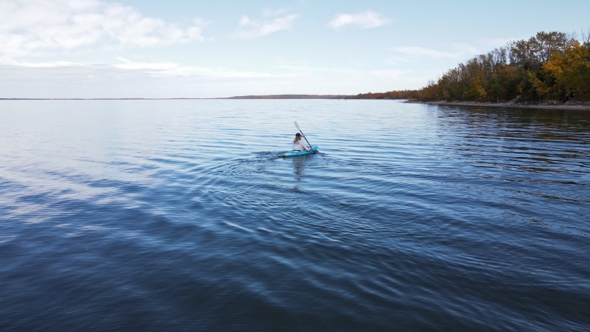 Clear blue buffalo lake in southern Alberta during autumn. Aerial footage of a person in a blue kayak paddling along