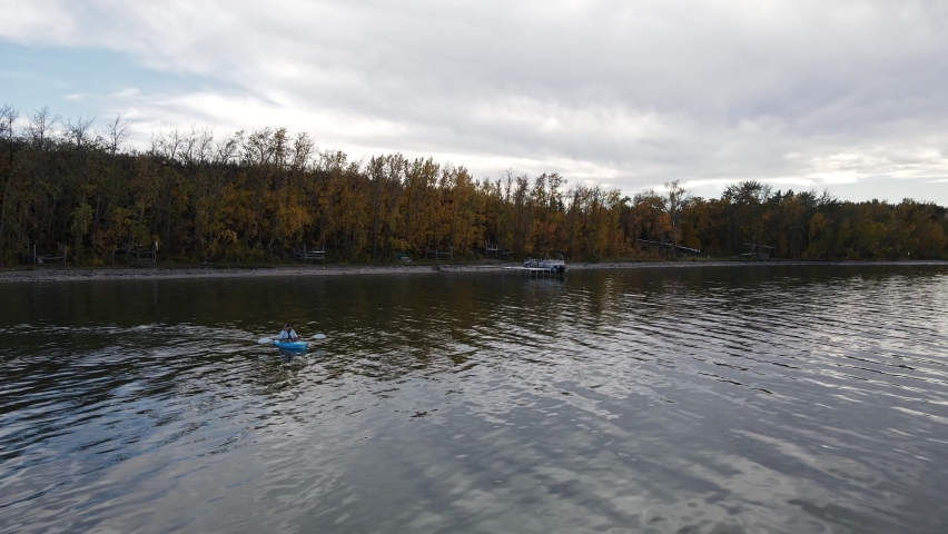 Young woman sitting in a small blue kayak paddling over Buffalo Lake on a cloudy autumn day. Aerial parallax shot