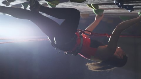 Bouldering, female professional climber training on a steep wall, practicing rock-climbing and moving up, using insurance, vertical video.