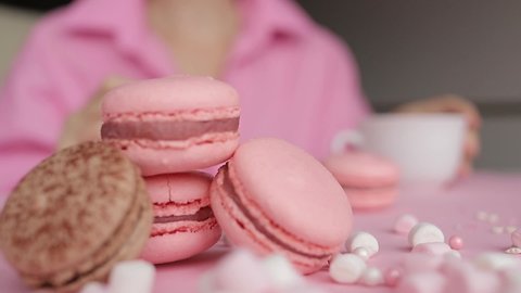 Woman in pink shirt eating pink macarons and drinking coffee. Holiday concept decoration. High quality FullHD footage.