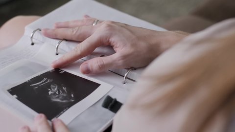 a pregnant woman opens a notebook and inserts an ultrasound photo into an album. Family values, a photo album with the first photo of the baby. 4k in slow motion