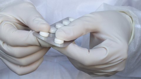 woman's (doctor, nurse) hands in gloves taking out pill from blister pack. medical assistant in white disposable robe is holding plastic blister with round tablets. Natural herbs, organic pills