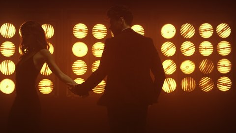 Passionate pair tenderly holding hands dancing near soft club lamps. Handsome guy touching woman palm walking away. Lovers saying goodbye diverging in different directions. Gentle movement in dance.