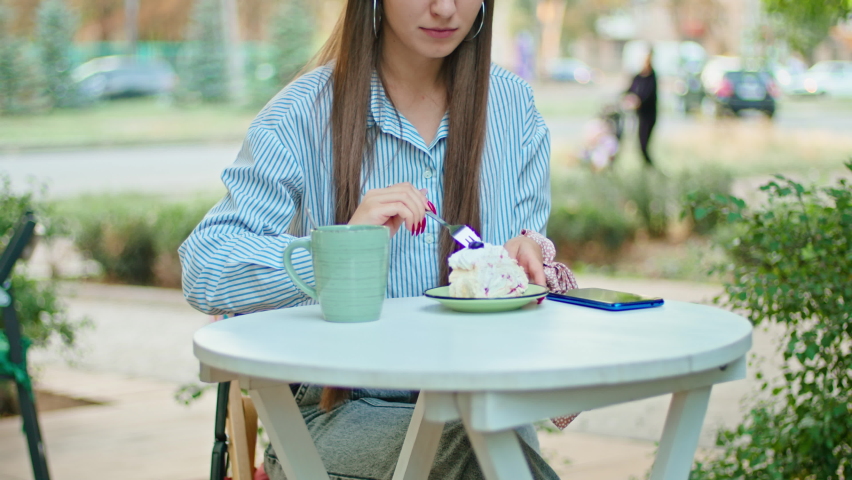 young happy woman in a street cafe eats a cake