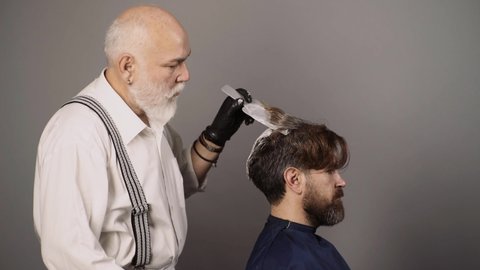 Hairdresser is dying male hair. Coloring man hair process. Man dyeing hair while using a brush. Colouring of gray hair at barber salon. Haircare and men hairstyling.