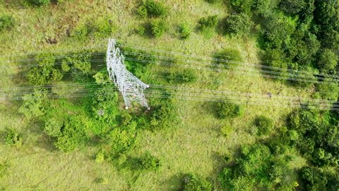 Aerial top down view high voltage steel power pylons in green field countryside. Flight over power transmission lines. Electric tower line, daylight, summer day