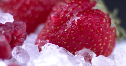 A drop of water dripping on a blackberry on ice with strawberries and raspberries on a black background. slow motion, filmed on high speed cinema camera, downscale, 4K.