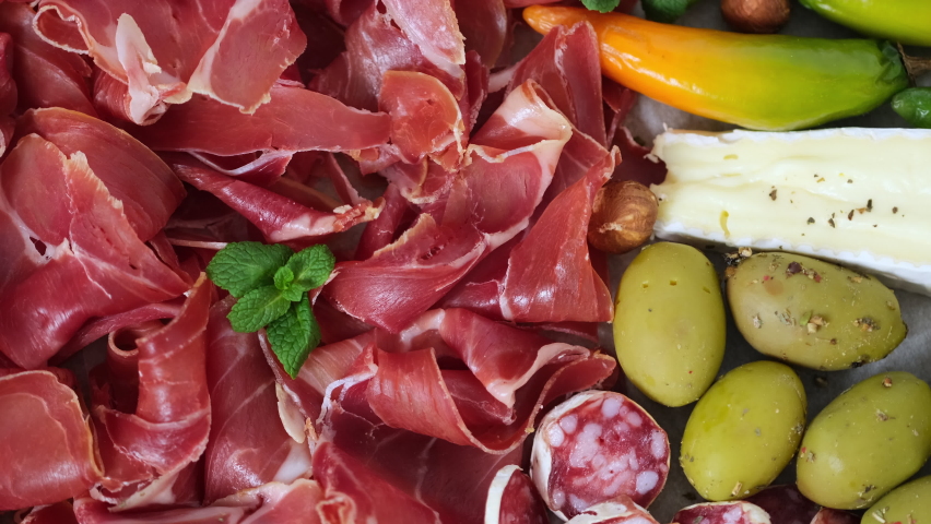 Meat appetizer selection - sliced prosciutto, sausage, ham, boiled pork, balyk, jamon, sandwich, cheese, salami, bread sticks, olives, tomatoes. Meat platter, Meat plate rotating View from above Slow 