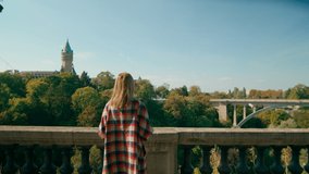 Young European Woman Takes Pictures, Photos or Films by Mobile Smart phone Landmark Adolphe Bridge in Luxembourg City. Tourism, Travel and Sightseeing concept. 4K medium zoom in shot