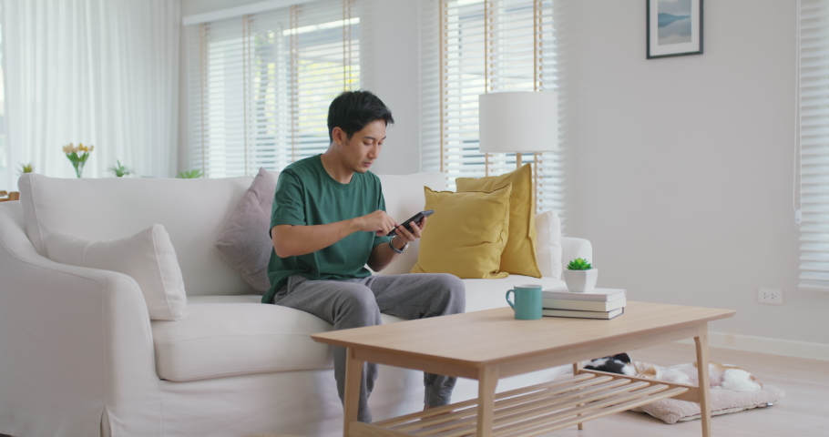 Asia young people teen man read good news message sitting at home sofa couch happy fun joy laugh smile in job hired result on mobile, award bonus, win online trade, sale order, loan money pay approve. | Shutterstock HD Video #1089027871