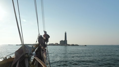 Front of the old sailing ship moving with the waves and old historical lighthouse in the background isolated at the sea