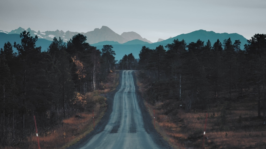 A narrow dirt road in the autumn landscape. Mountains on the horizon. Slow-motion, pan forward.