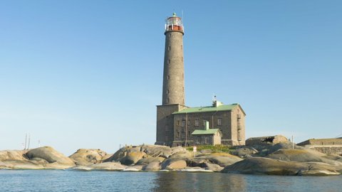 Historical lighthouse made of grey stone in finnish archipelago filmed from the side on a moving boat
