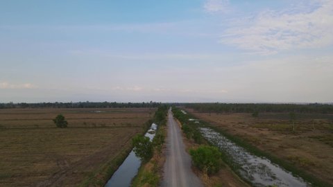Aerial reverse footage of a provincial farm road revealing canals and grassland, Pak Pli, Nakhon Nayok, Thailand.
