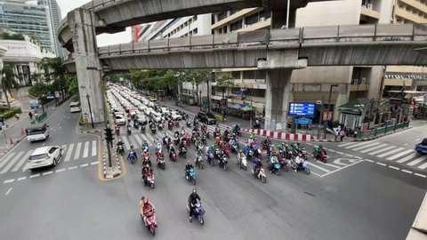 BANGKOK, THAILAND - Circa November, 2021: Motorcycles Traffic at intersection top view near Central World Shopping Plaza Complex, famous tourist attraction on Ratchadamri Road. Sky train track above