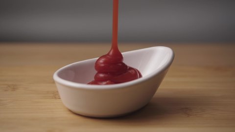 Ketchup being squeezed out of bottle. stock footage. Close-up of jet of red ketchup on gray background. pouring for white sauce. white sauce pouring into bowl. Ketchup spills out of large red bottle