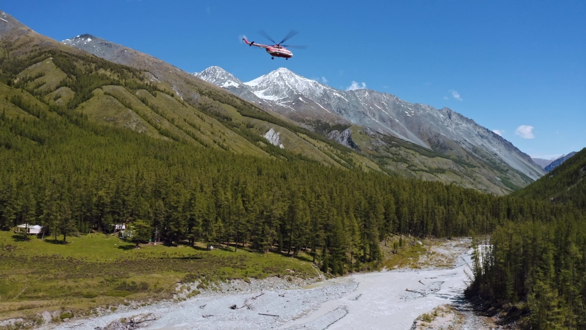Aerial shot of helicopter flying over trees. Drone Shot .Helicopter low flying in blue sky with green forest on mountains in background. Royalty-Free Stock Footage #1089036205